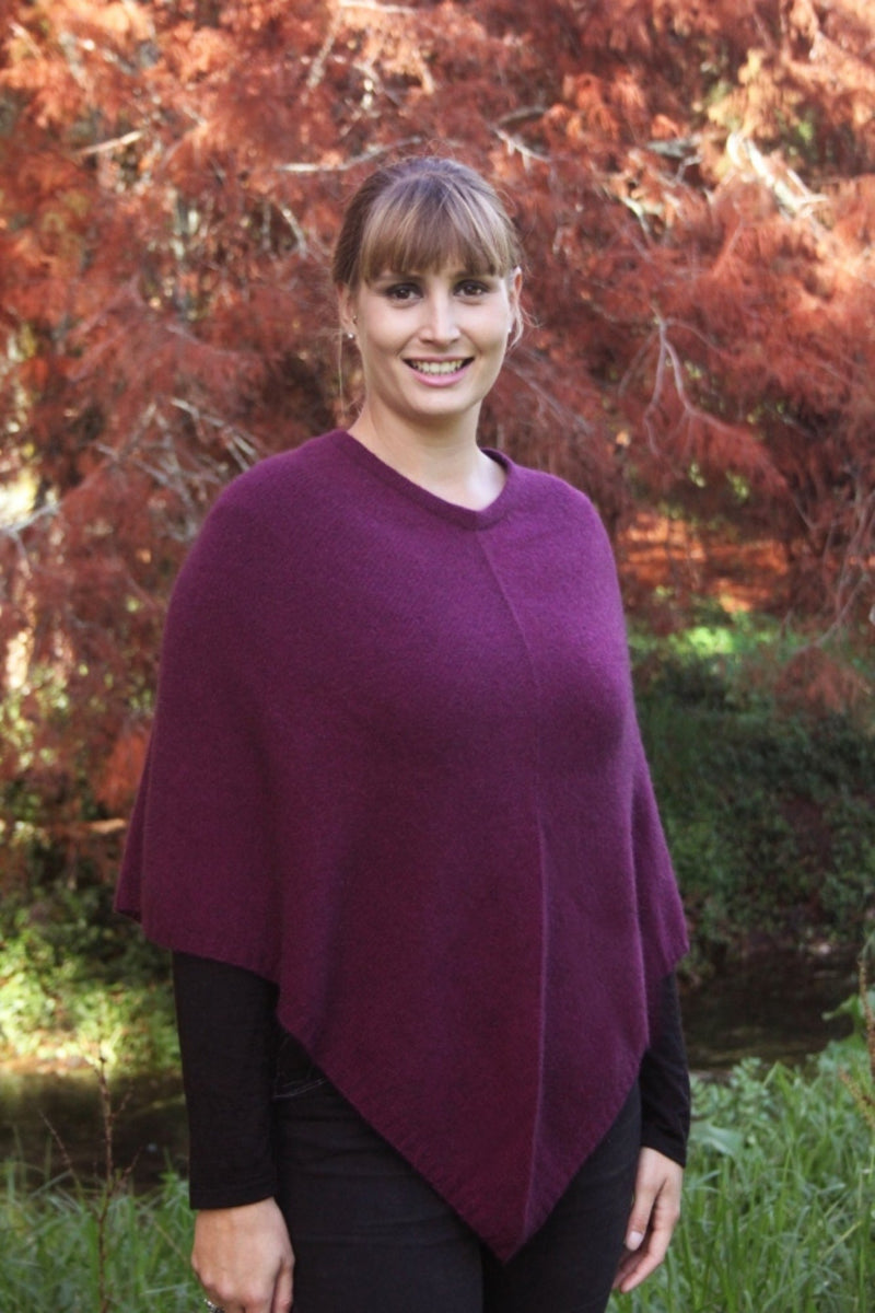 Berry purple possum and merino wool poncho on female model standing in garden. Warm, soft, lightweight possum and merino wool. Lothlorian