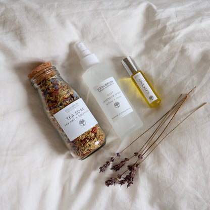 Equilibrium aromatherapy sleep pack including a sleep lavender spray, tea soak bath salts and lavender perfume in glass roll on with twigs of lavender laying on white pillow