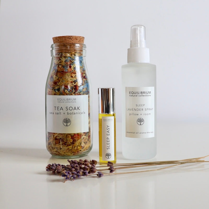 Equilibrium aromatherapy sleep pack including a sleep lavender spray, tea soak bath salts and lavender perfume in glass roll on with twigs of lavender sitting on white table with white background