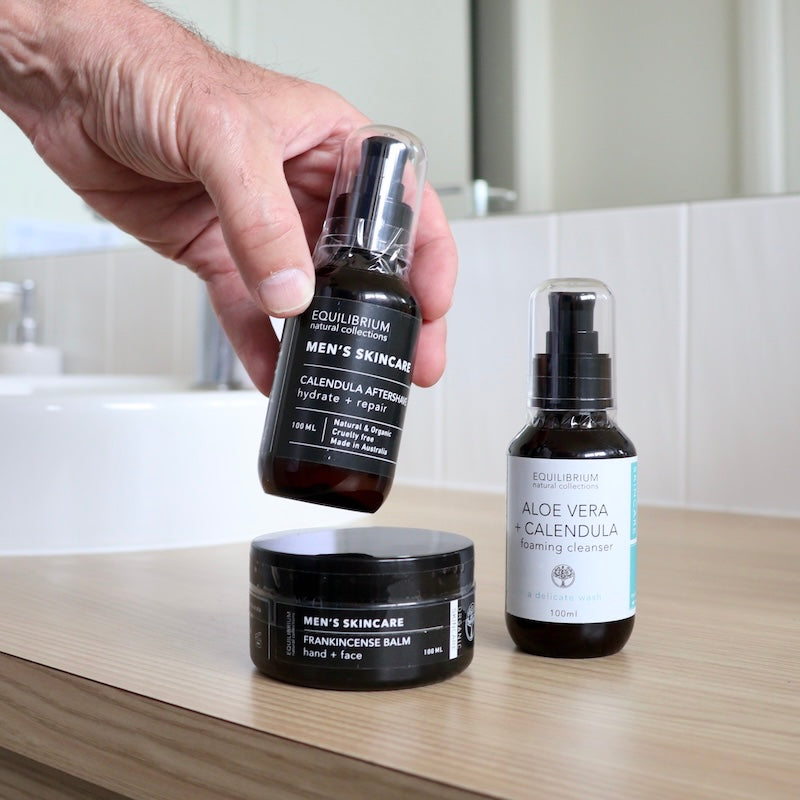 equilibrium mens skincare pack including hand & face balm, foaming cleanser in bottle sitting on a towel and aftershave in bottle being held by man