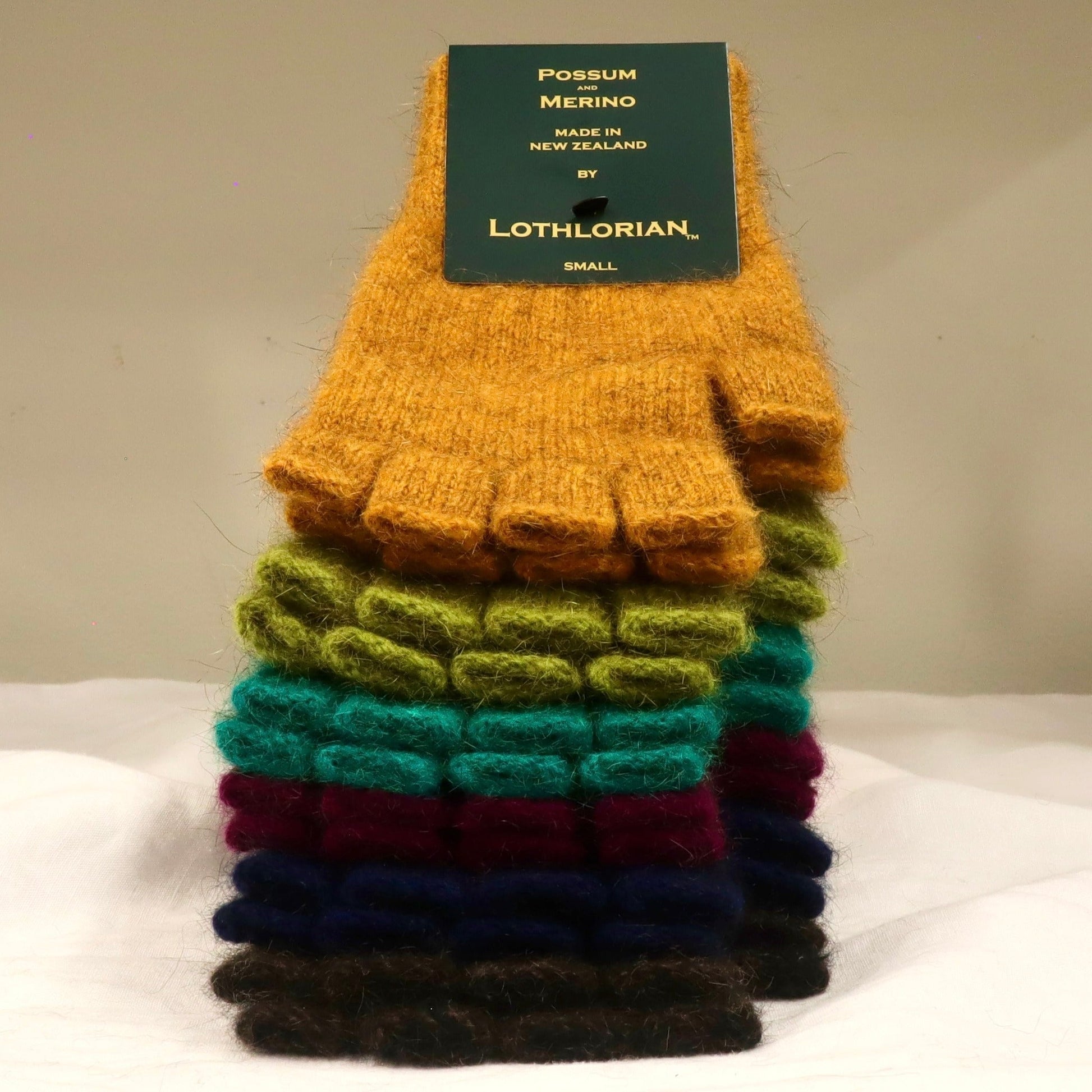 Fingerless possum merino wool gloves in a stack on table showing multiple colours