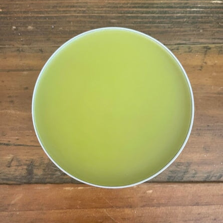 Green hemp healing balm in tin with lid off showing balm sitting on table