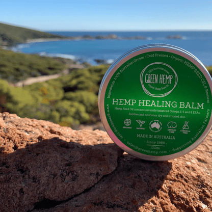 Hemp healing balm with green label on tin sitting on rock in front of ocean