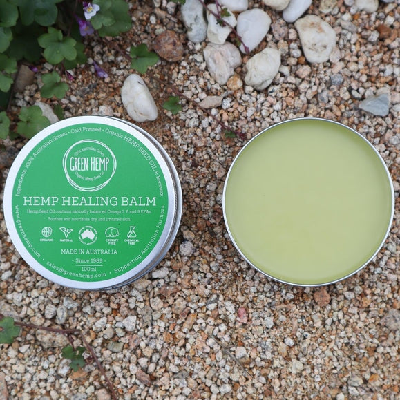 Green Hemp healing balm in tin with lid off sitting on ground showing balm inside